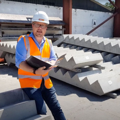 Mark Ellis poses with book in front of precast concrete stair units